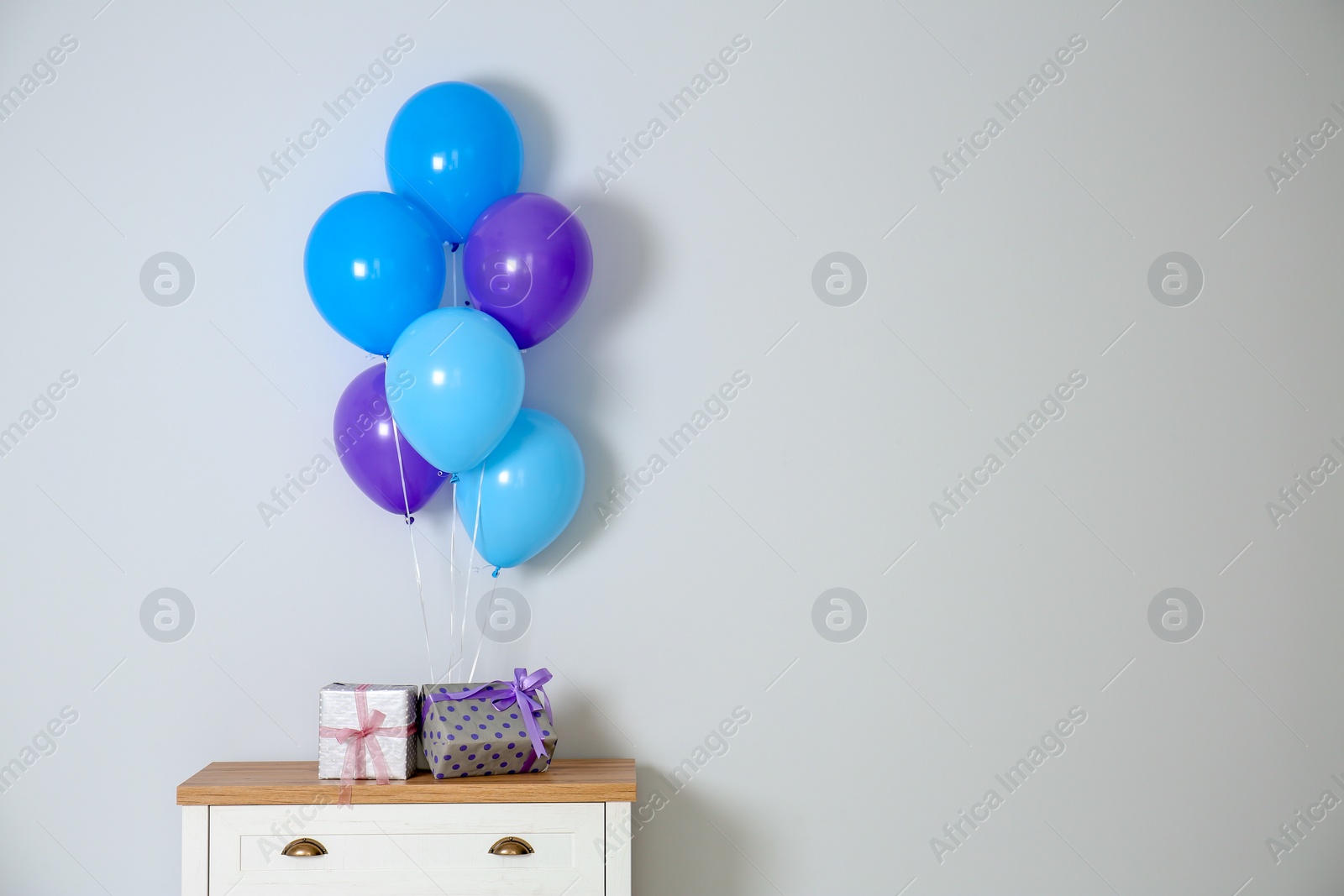 Photo of Bunch of bright balloons and gifts on table against white wall. Space for text