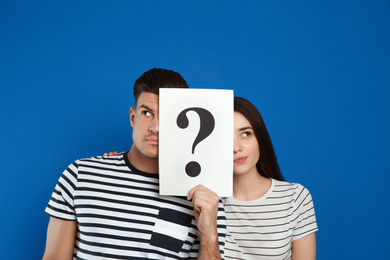 Photo of Couple holding question mark sign on blue background