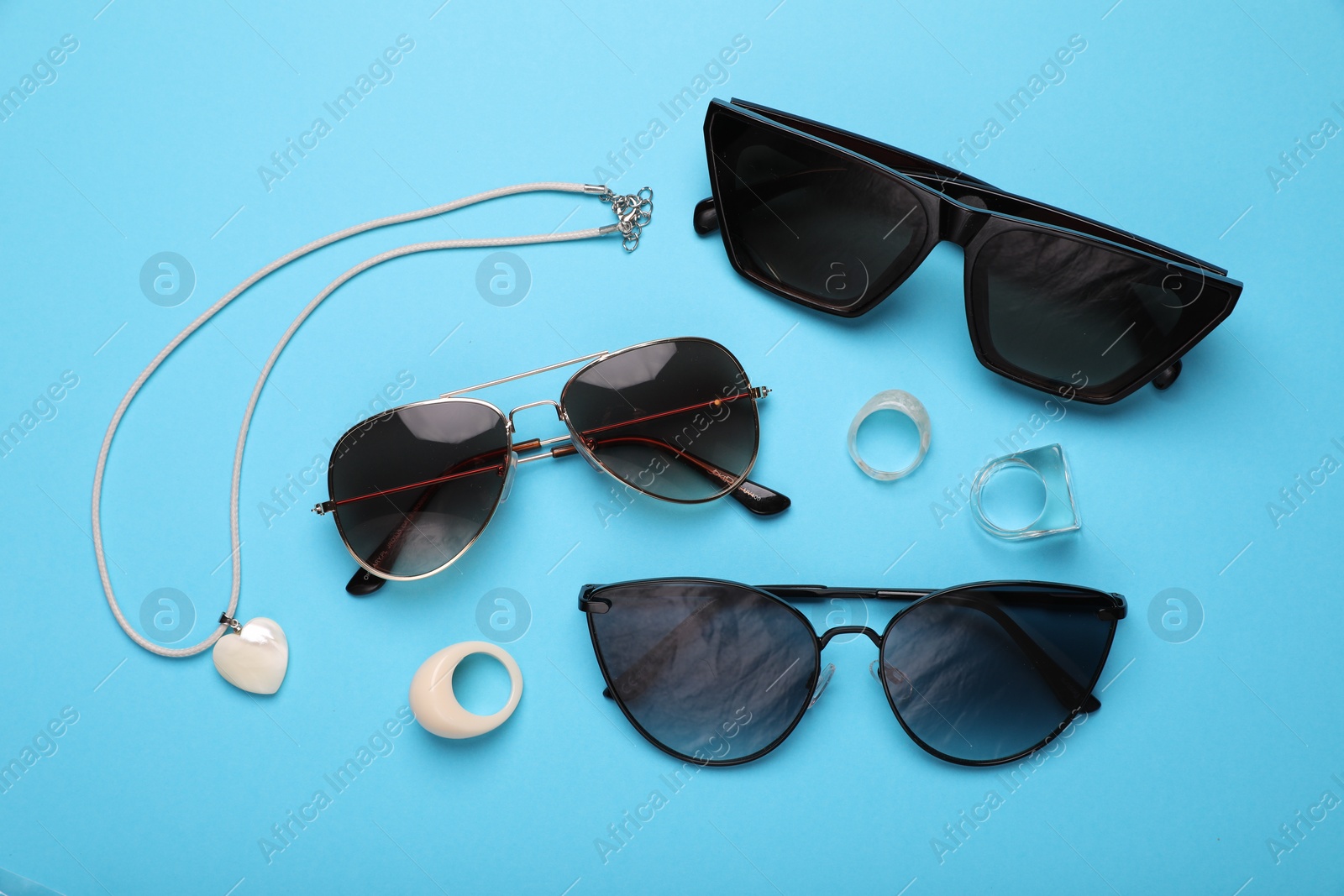 Photo of Stylish sunglasses and accessories on light blue background, flat lay