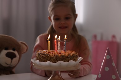 Photo of Cute girl with birthday cake at table indoors, focus on burning candles
