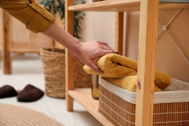 Woman putting towel into storage basket indoors, closeup