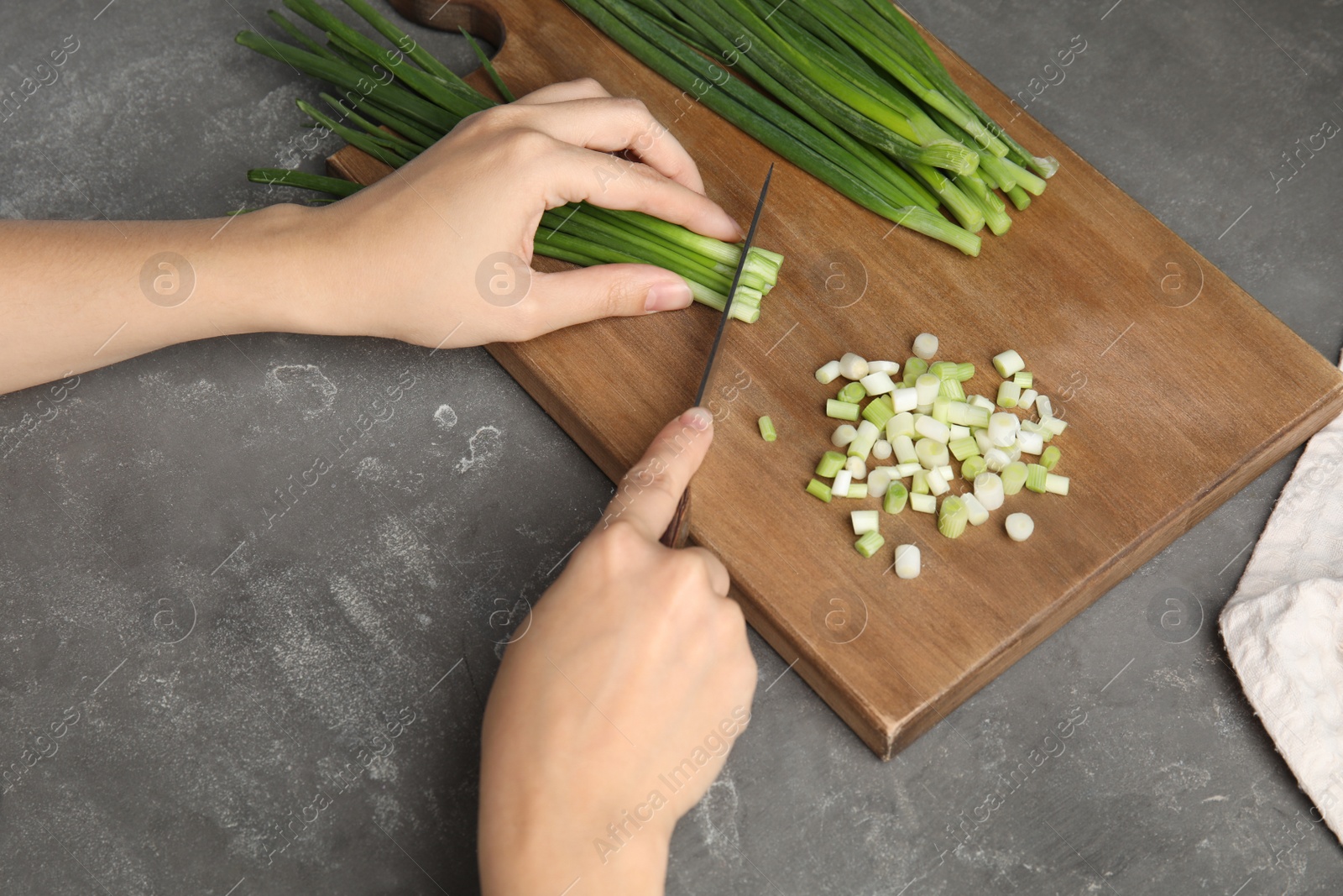 Photo of Woman cutting fresh green onion on wooden board