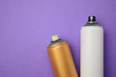 Cans of different graffiti spray paints on violet background, flat lay. Space for text