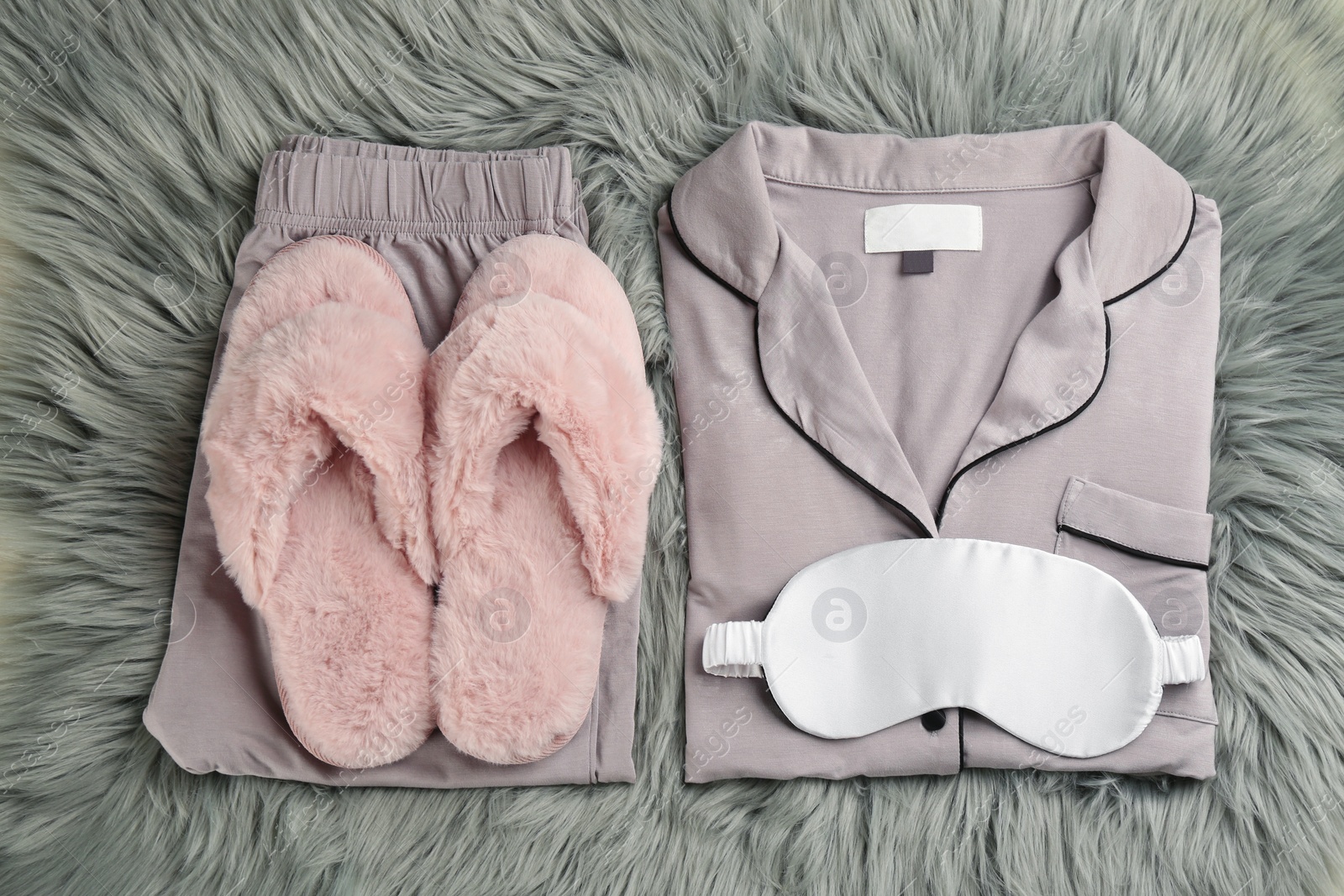 Photo of House slippers, sleeping mask and pajamas on grey faux fur, flat lay