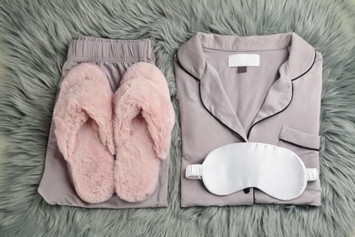 Photo of House slippers, sleeping mask and pajamas on grey faux fur, flat lay