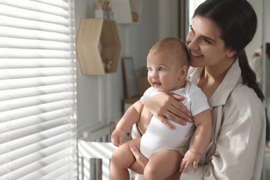Photo of Happy young mother with her baby near window at home. Space for text