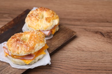 Photo of Delicious bagels with ham and cheese on wooden table. Space for text