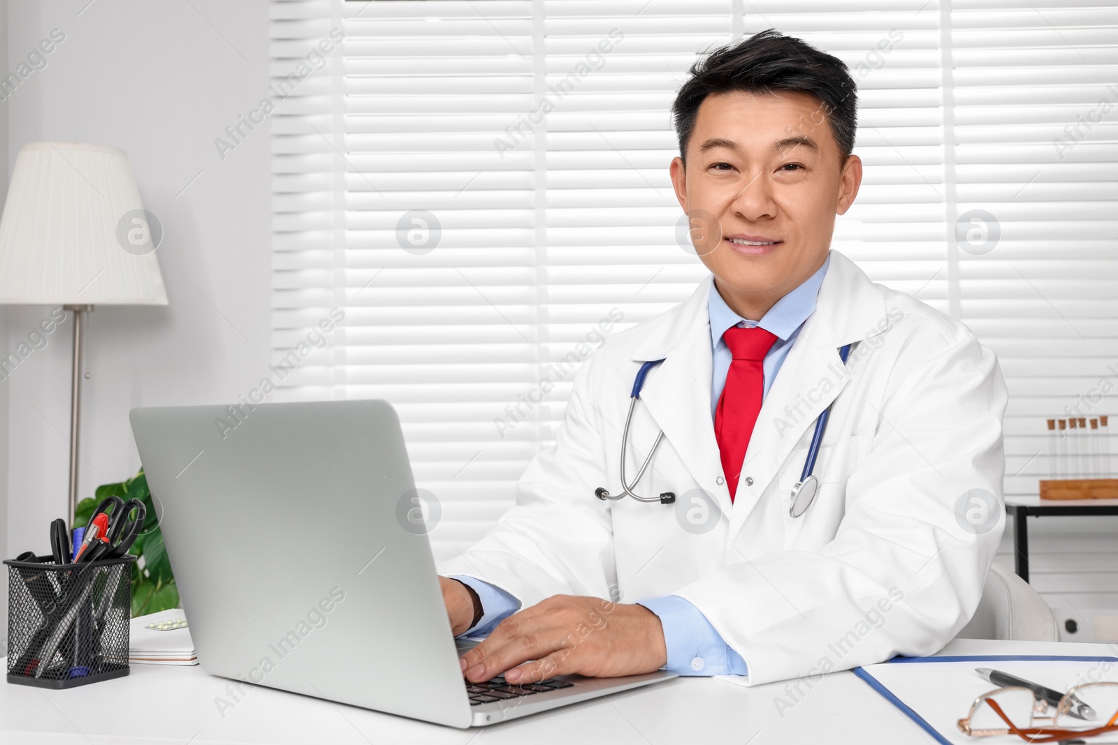 Photo of Happy doctor with laptop consulting patient at white desk in clinic. Online medicine