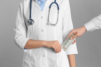 Photo of Patient putting bribe into doctor's pocket on grey background, closeup. Corruption in medicine