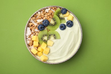 Photo of Tasty matcha smoothie bowl served with fresh fruits and oatmeal on green background, top view. Healthy breakfast