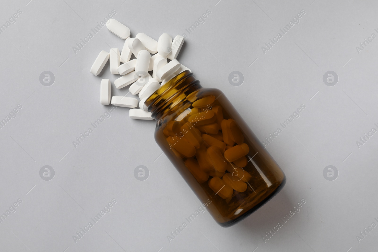 Photo of Vitamin pills and bottle on light grey background, top view