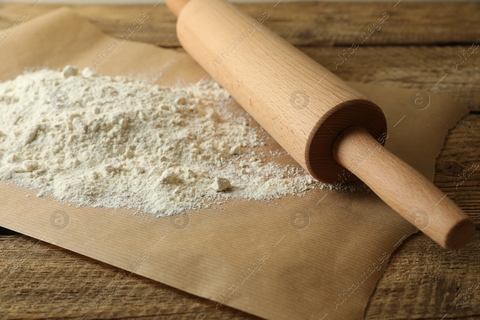 Photo of Parchment with flour and rolling pin on wooden table, closeup