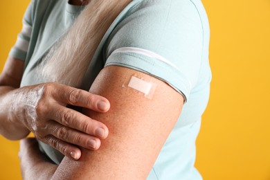 Photo of Mature woman showing arm with bandage after vaccination on yellow background, closeup