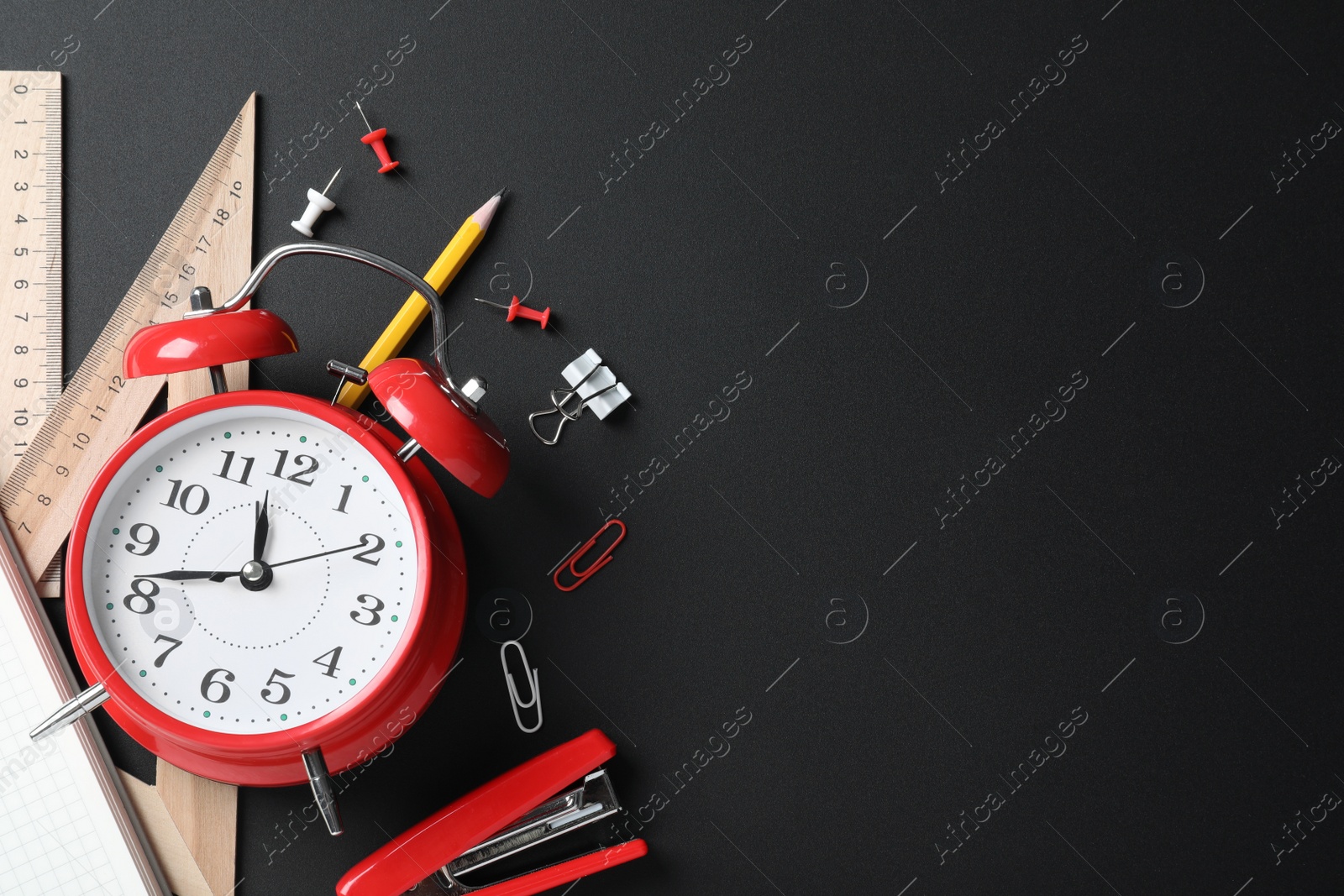 Photo of Flat lay composition with alarm clock and different stationery on black background, space for text. School time