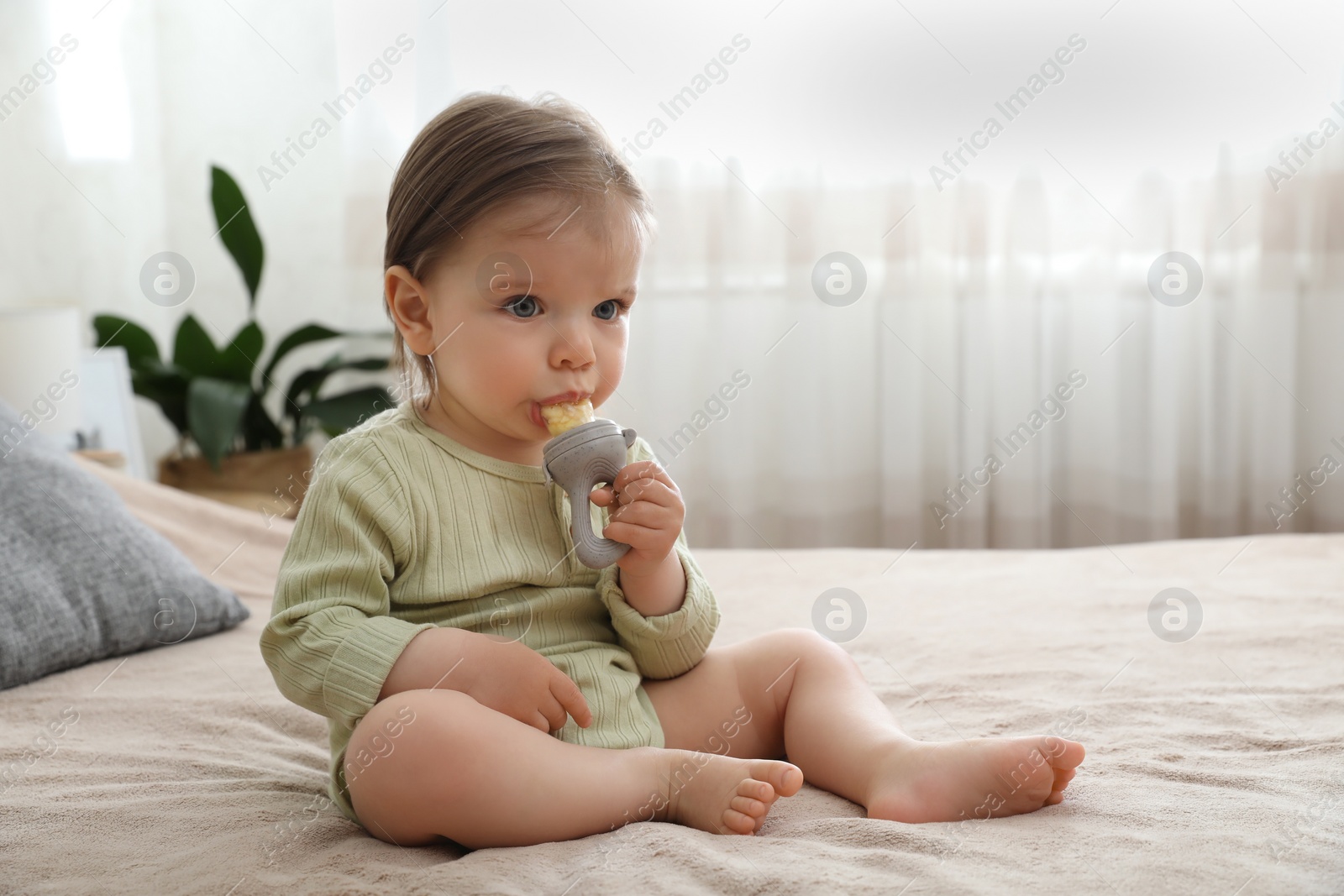 Photo of Cute baby girl with nibbler on bed at home. Space for text