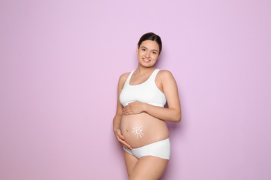 Sun painted with body cream on pregnant woman's belly against color background