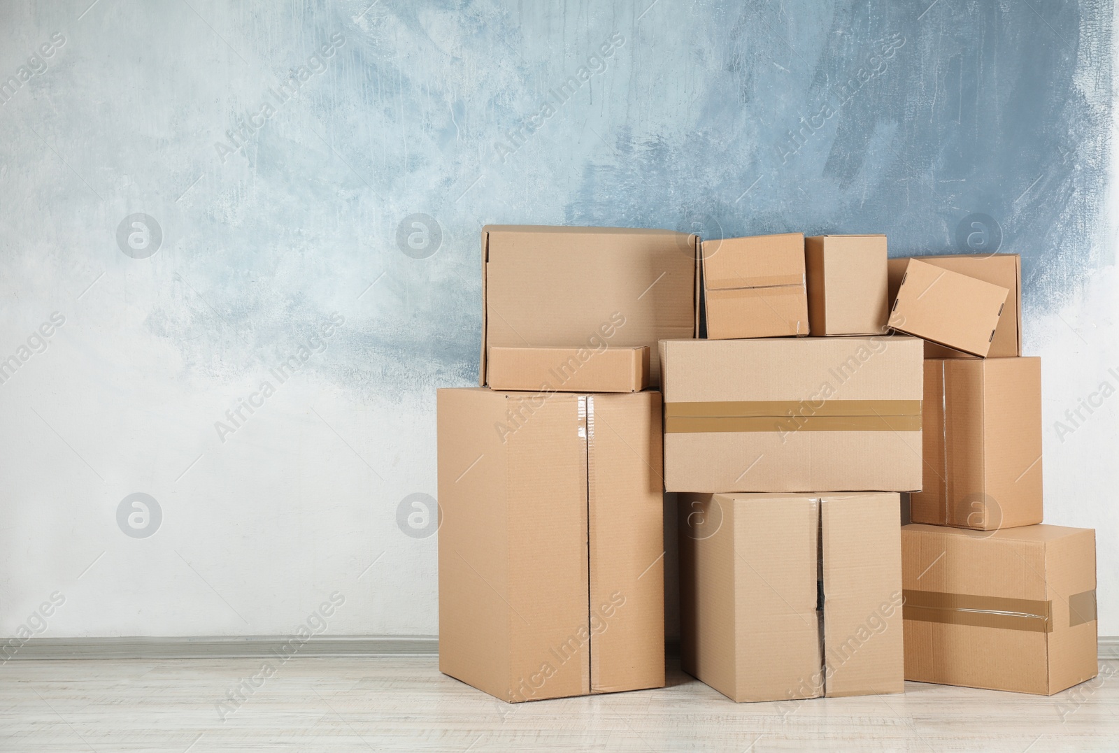 Photo of Pile of cardboard boxes near color wall indoors. Space for text