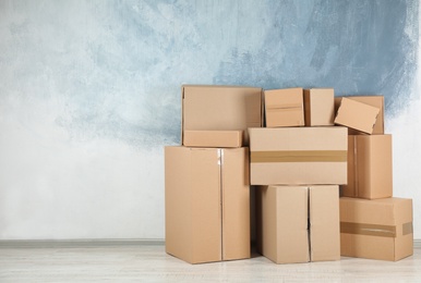 Photo of Pile of cardboard boxes near color wall indoors. Space for text