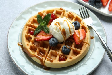 Photo of Delicious Belgian waffles with ice cream, berries and caramel sauce served on grey table, closeup