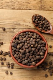 Photo of Aromatic allspice pepper grains in bowl and spoon on wooden table, top view