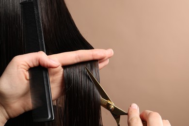 Photo of Hairdresser cutting client's hair with scissors on light brown background, closeup. Space for text