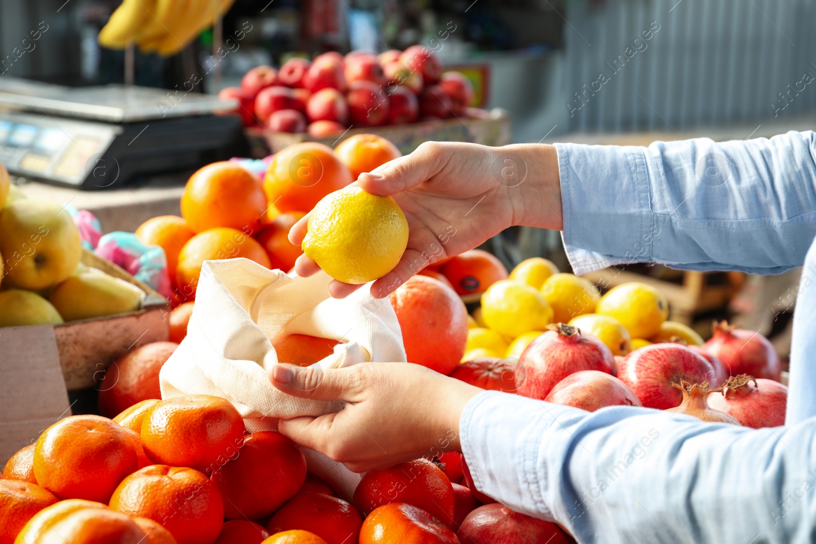 Photo of Woman putting lemon into cotton eco bag at wholesale market, closeup. Life without plastic