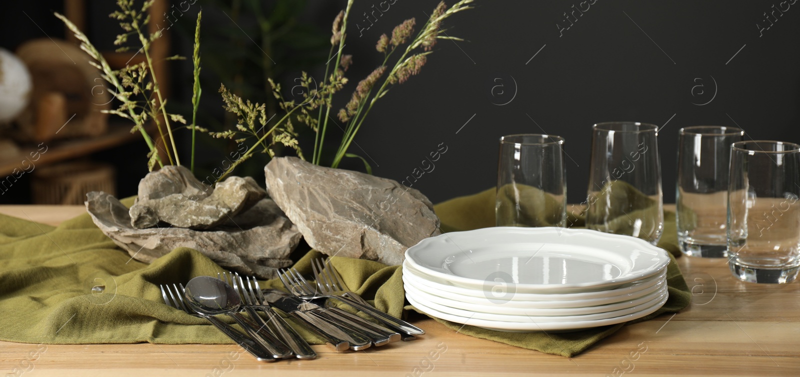 Photo of Clean dishes, stones and plants on wooden table in dining room