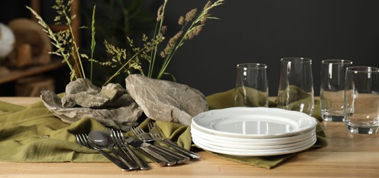 Photo of Clean dishes, stones and plants on wooden table in dining room