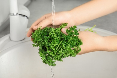 Photo of Woman washing fresh parsley under tap water in kitchen sink, closeup