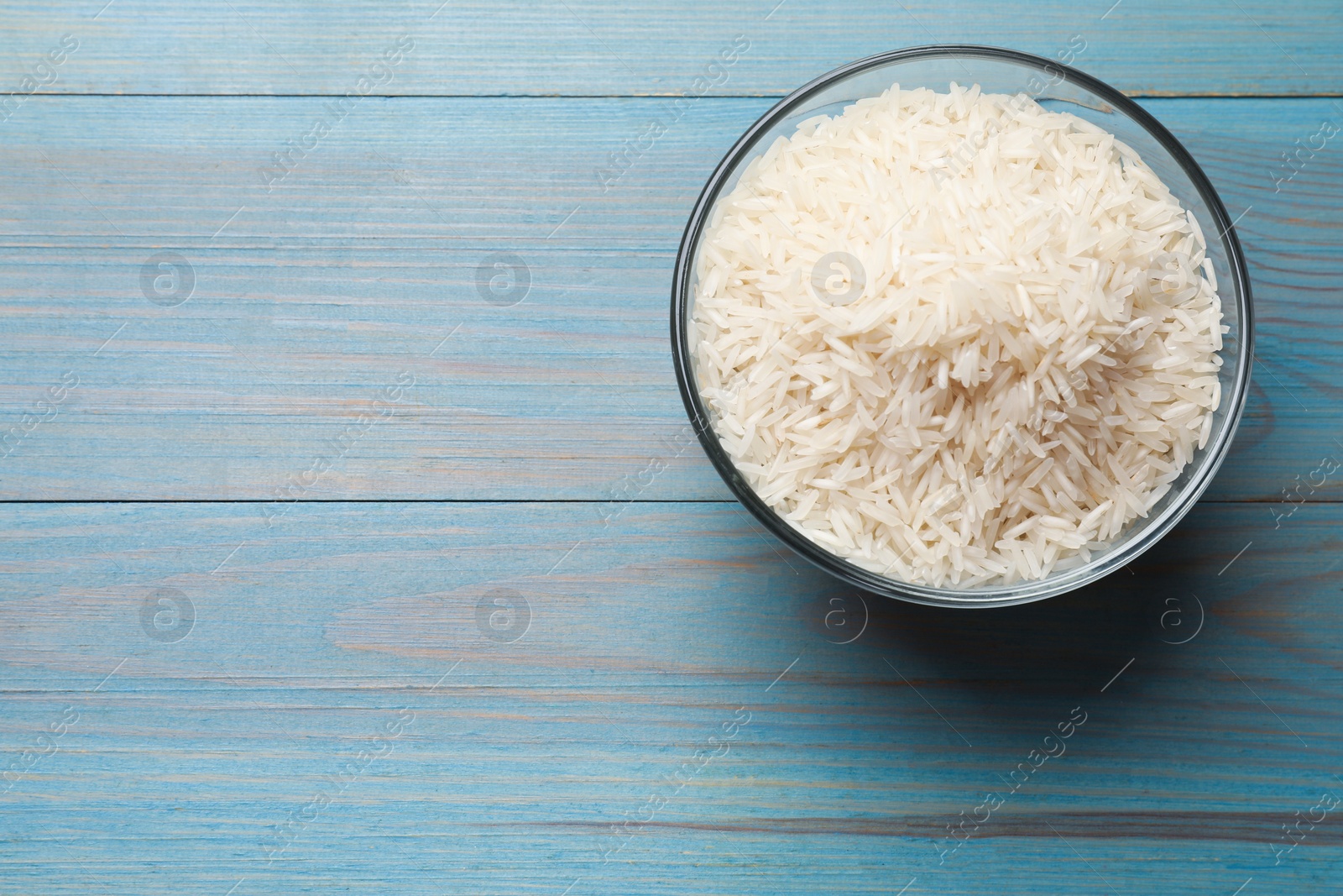 Photo of Raw basmati rice in bowl on light blue wooden table, top view. Space for text