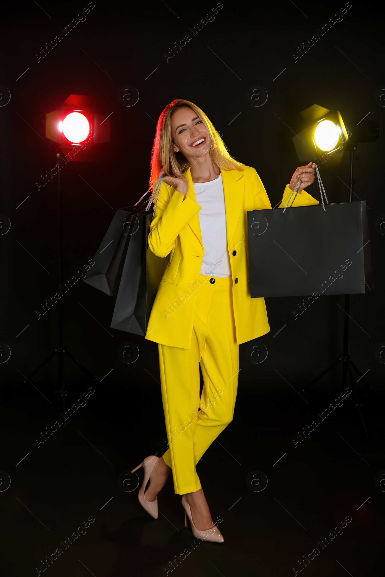 Photo of Happy young woman with shopping bags on dark background. Black Friday Sale