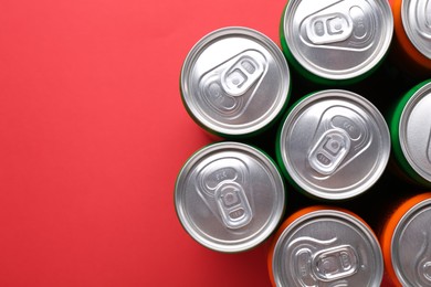 Energy drink in cans on red background, top view. Space for text