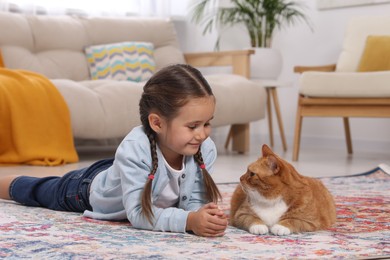Photo of Smiling little girl and cute ginger cat on carpet at home