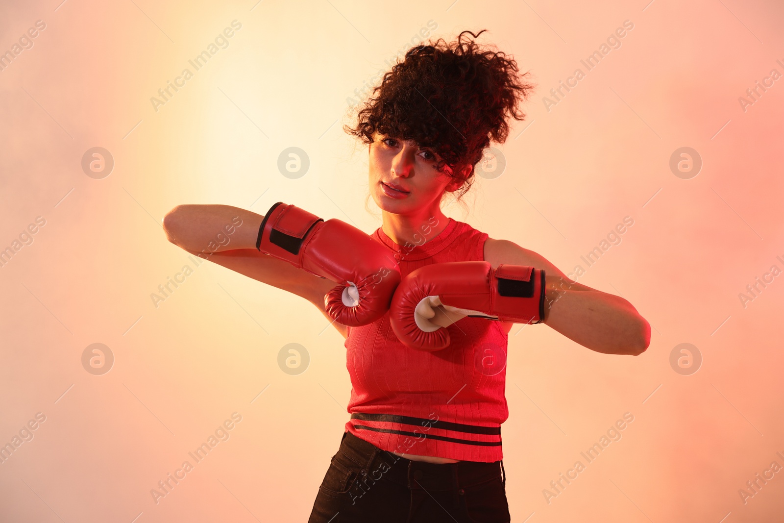 Photo of Beautiful young woman with boxing gloves on color background in neon lights