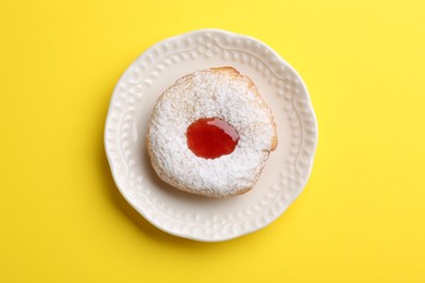 Photo of Hanukkah donut with jelly and powdered sugar on yellow background, top view