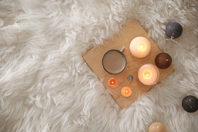 Wooden board with burning candles on faux fur, top view