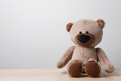 Photo of Cute teddy bear on wooden table near light wall, space for text