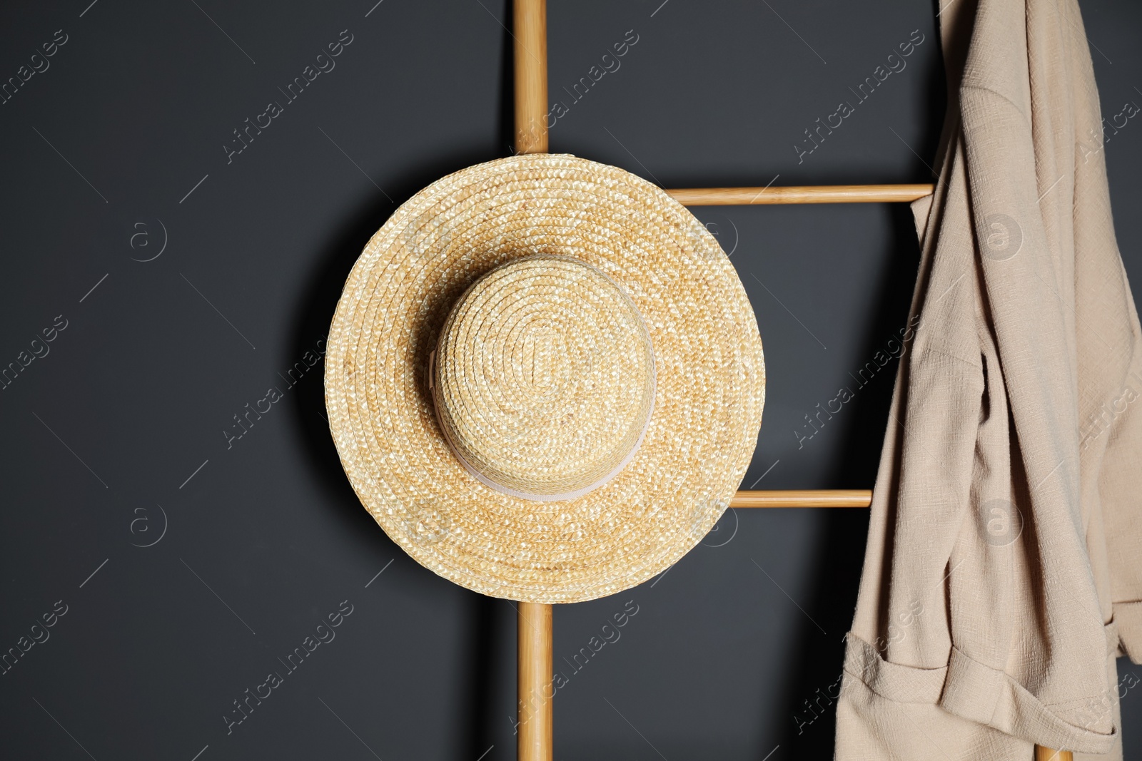 Photo of Straw hat and jacket on ladder near dark wall