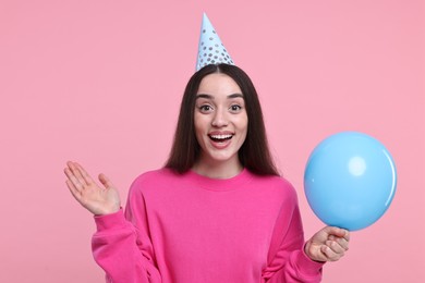 Happy woman in party hat with balloon on pink background