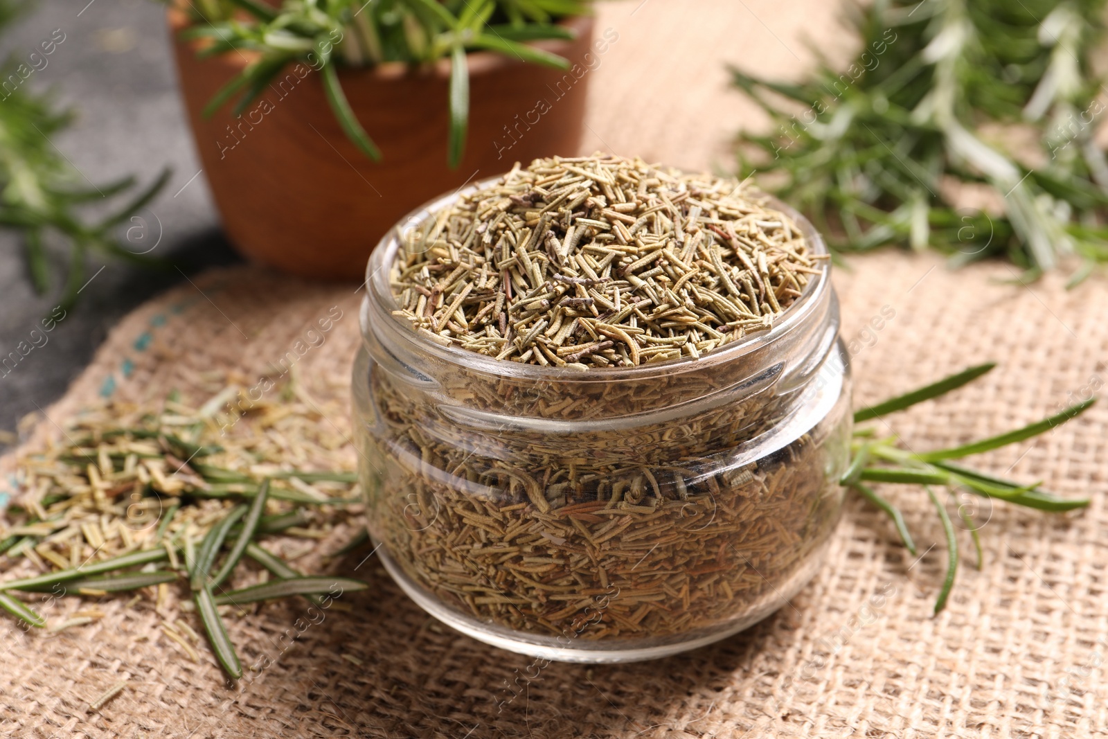 Photo of Jar with dry rosemary on burlap fabric, closeup