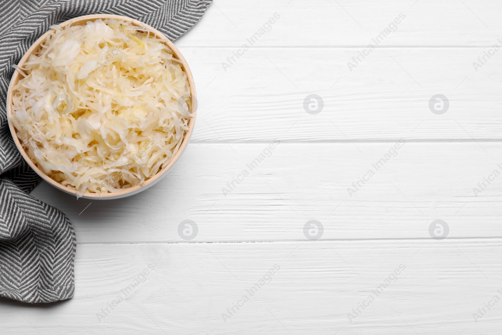 Photo of Bowl of tasty sauerkraut on white wooden table, flat lay. Space for text