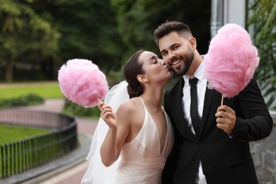 Photo of Happy newlywed couple with cotton candies outdoors