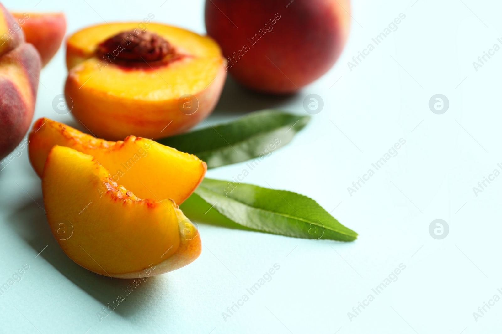 Photo of Slices of fresh ripe peach and green leaves on light blue background, closeup. Space for text