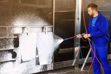 Worker cleaning auto mats with high pressure foam jet at car wash