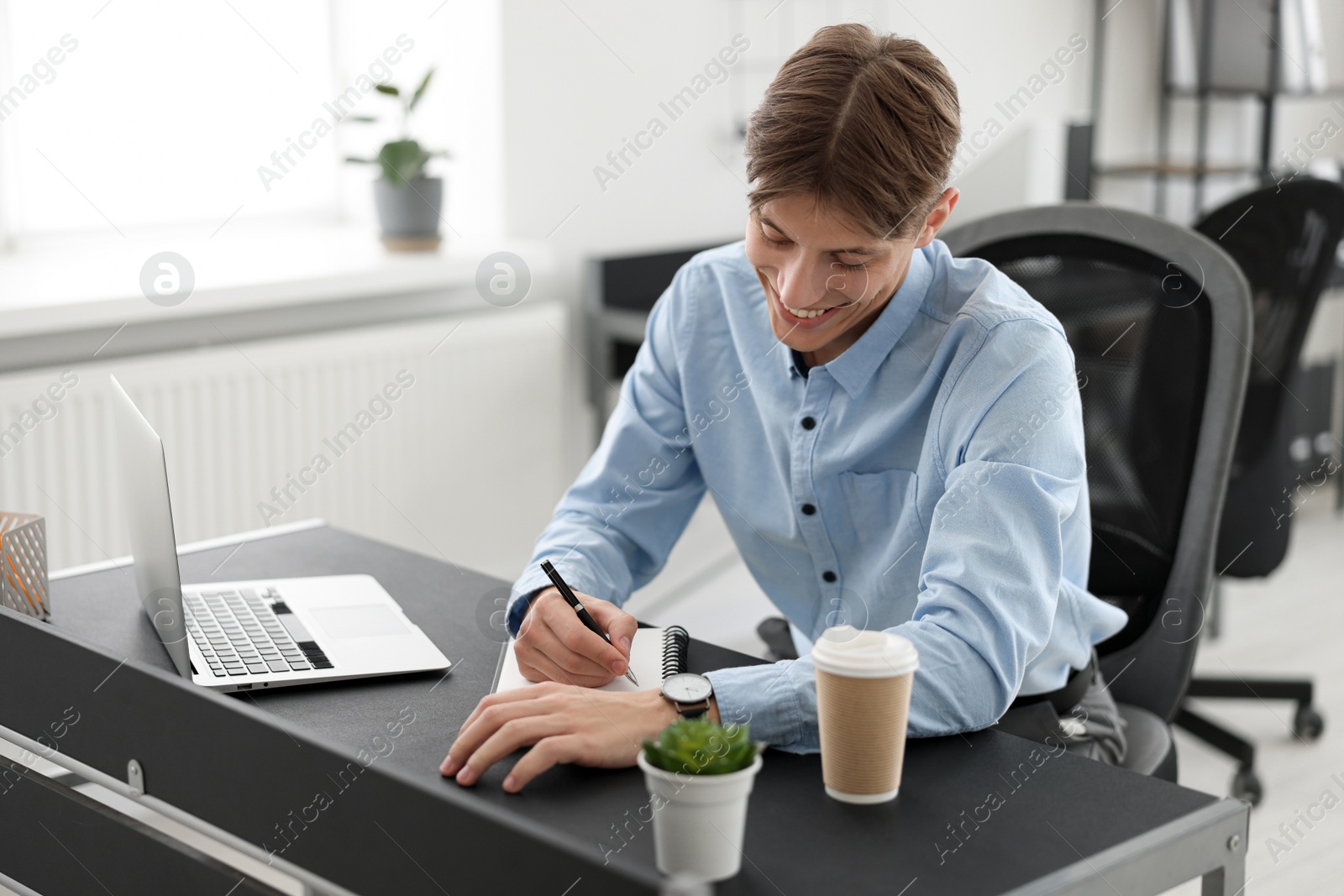 Photo of Man taking notes during webinar at table in office