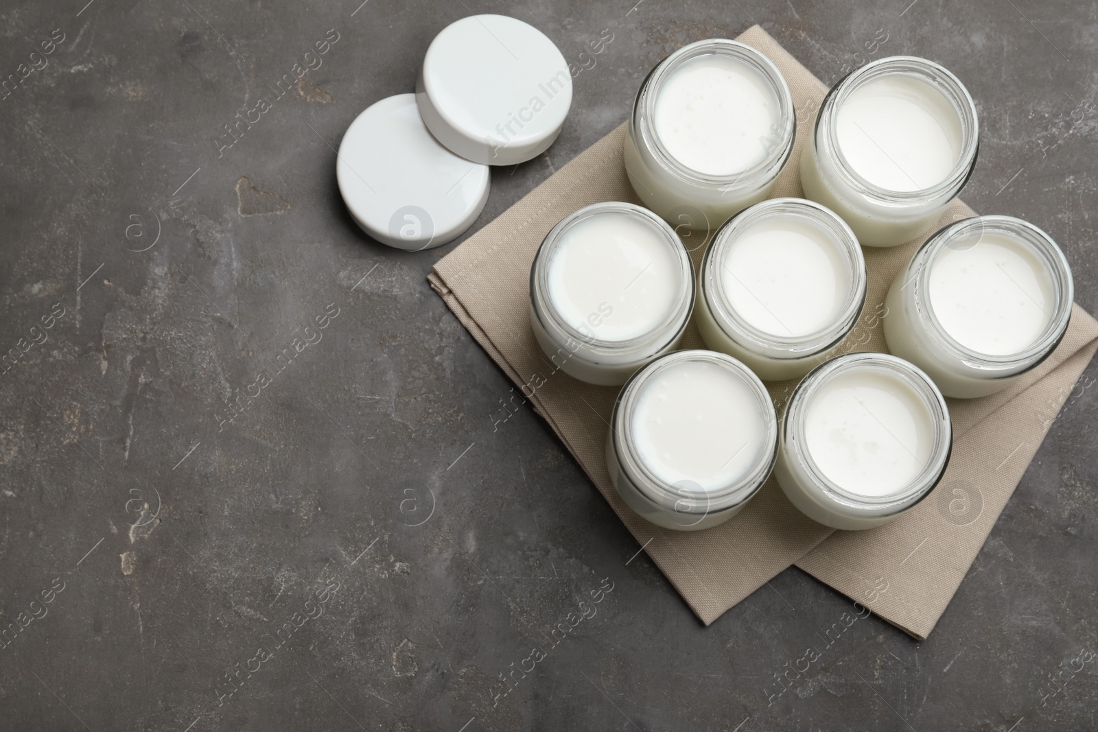 Photo of Tasty yogurt in glass jars on grey table, flat lay. Space for text