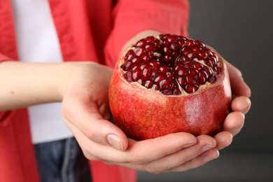 Photo of Woman holding fresh pomegranate on grey background, closeup