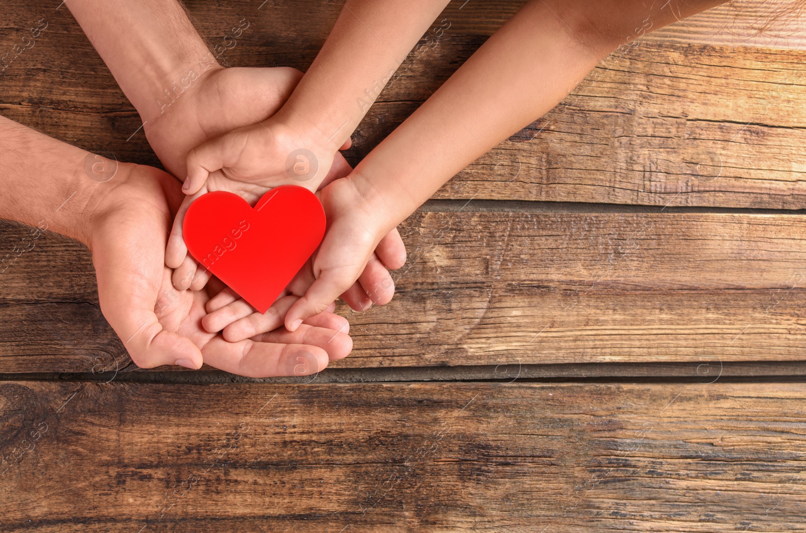 Photo of Family holding small red heart in hands on wooden background