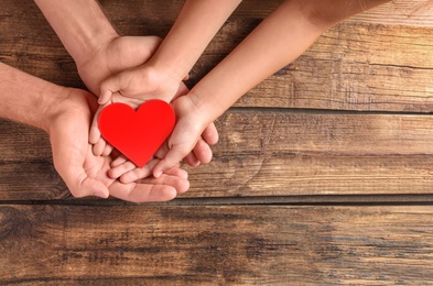 Photo of Family holding small red heart in hands on wooden background