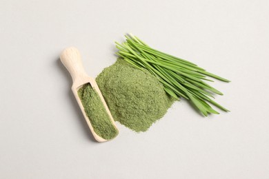 Pile of wheat grass powder, scoop and fresh sprouts on light table, flat lay